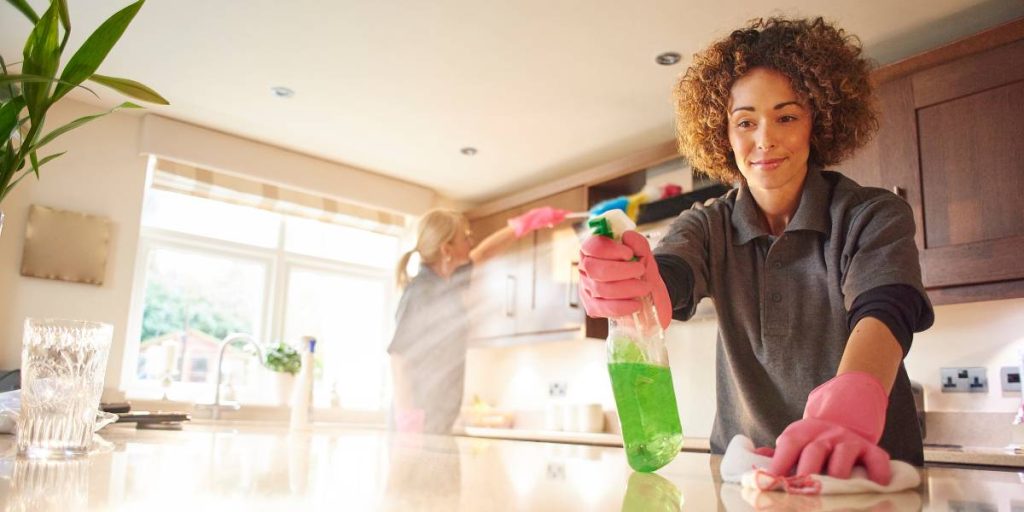 Professional maid spraying cleaning solution onto a kitchen countertop.