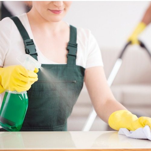 A professional cleaner spraying cleaning solution onto a countertop and wiping it with a microfiber cleaning cloth.