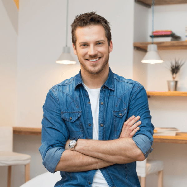 A man wearing a denim button-up shirt smiling with his arms crossed in front of his chest.